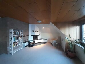 Ein modernes Wohnzimmer mit Kamin, Bücherregal, Essbereich und großem Fenster.
