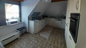 A compact kitchen with a sloped ceiling, white cabinetry, a built-in stove, and a microwave. - Spacious apartment for up to 8 people - family-friendly, pets welcome (Schneverdingen)
