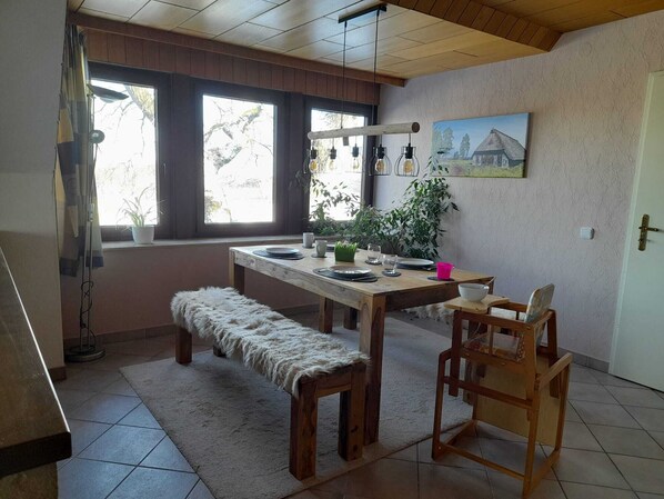 Ein gemütlicher Essbereich mit Holztisch, einer Bank und Stühlen, einem Fenster mit Vorhängen sowie einem Bild an der Wand.