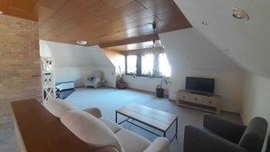 A spacious living area with a high ceiling, a sofa, a coffee table, and a TV stand. - Spacious apartment for up to 8 people - family-friendly, pets welcome (Schneverdingen)