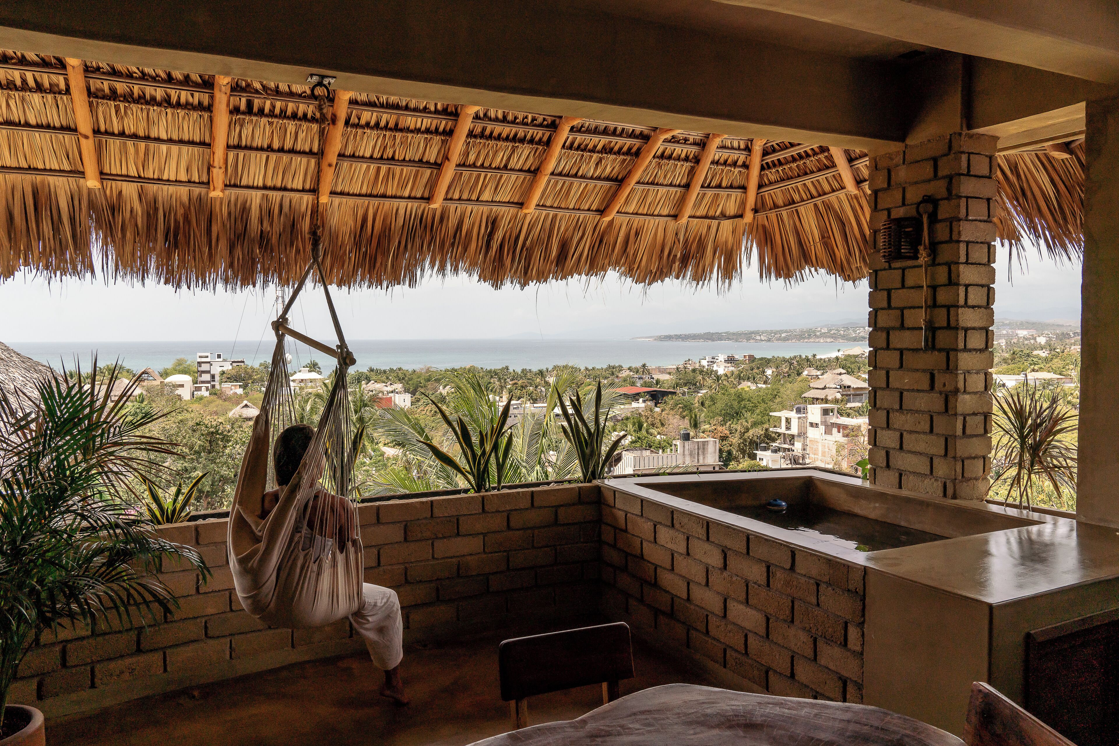 A room with a view of the sea, a hanging chair, a brick wall, and a small sink.