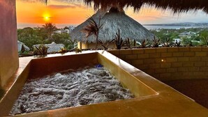 Un jacuzzi con vista a un atardecer y una estructura de techo de paja.