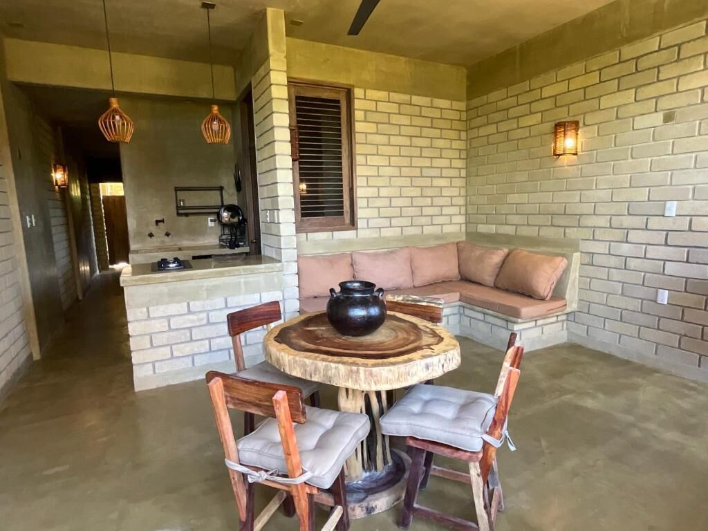 A cozy living area with a round wooden table, cushioned chairs, a sofa, and a brick wall.