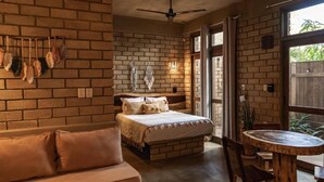 Un dormitorio con pared de ladrillo, una cama, un banco, una mesa y un ventilador de techo.