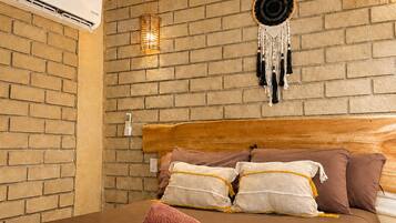 A bedroom with a brick wall, a wooden headboard, and a bed with multiple pillows and a rolled-up towel.