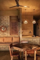Un interior acogedor con pared de ladrillo, banco de madera, mesa redonda de madera y lámparas colgantes.