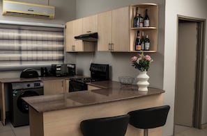 A modern kitchen with wooden cabinets, a built-in oven, a coffee machine, and a wine rack.