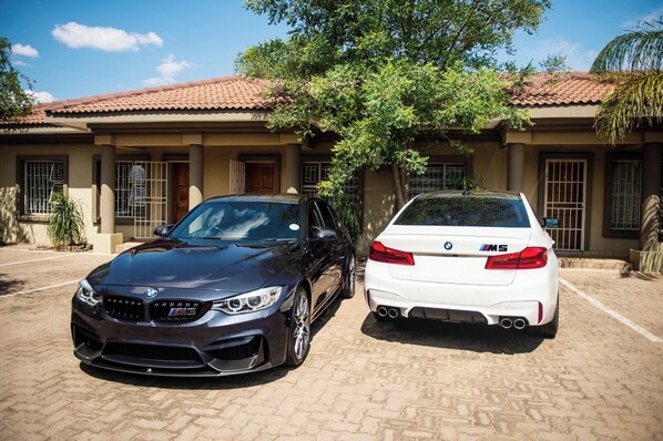 Two cars parked in front of a building with a tiled roof and a tree in the background.