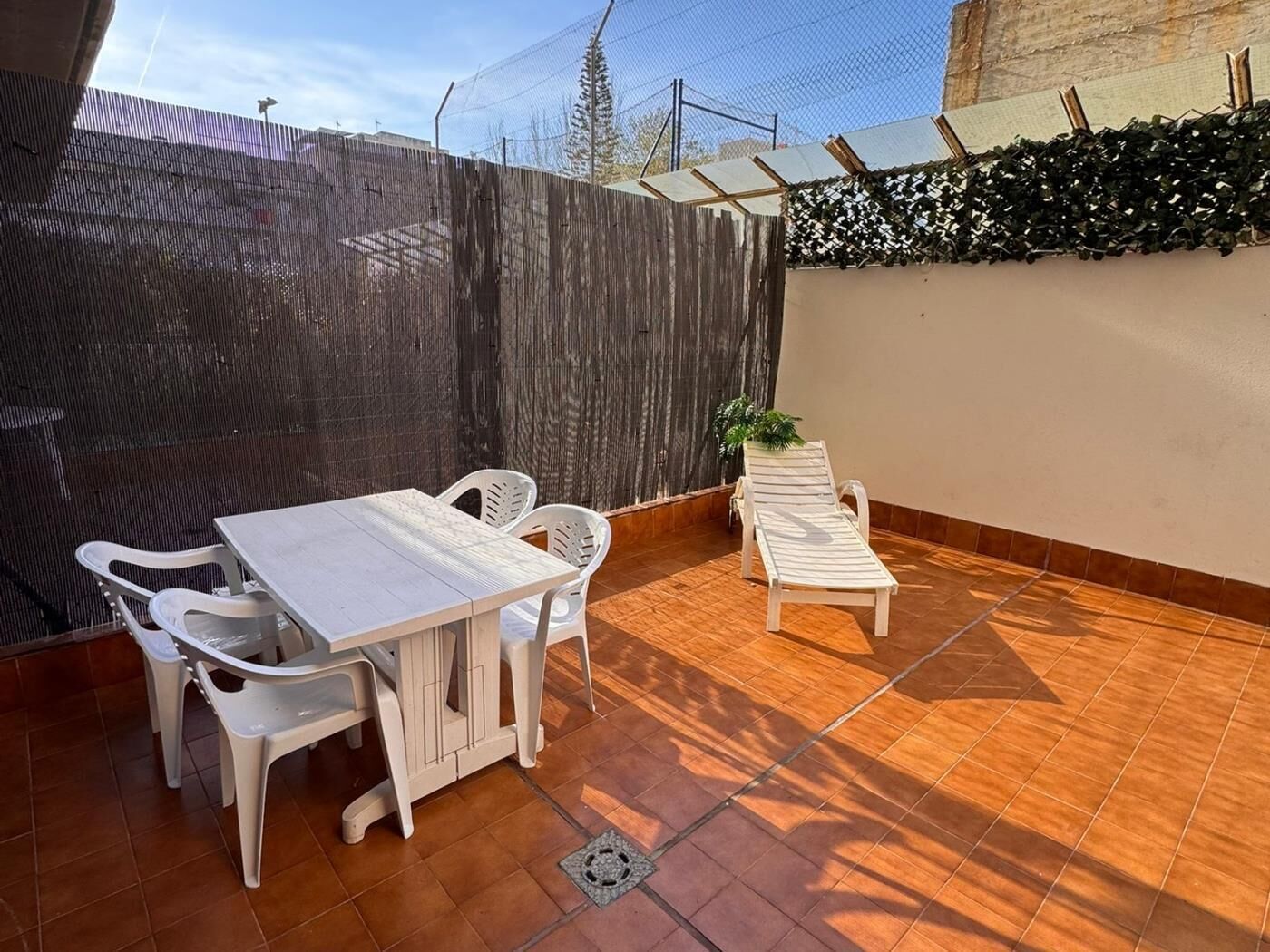 A patio with a table and chairs, a sun lounger, and a decorative wall.