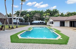 A rectangular swimming pool with a surrounding grassy area and paved walkway. - El bosque encantado (Miami)