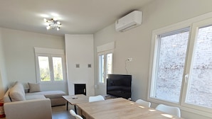 Un salon moderne avec une table à manger en bois, des chaises blanches, un canapé gris et un téléviseur à écran plat.