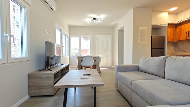 Un salon moderne avec un canapé, un téléviseur et un coin repas comprenant des chaises et une table.