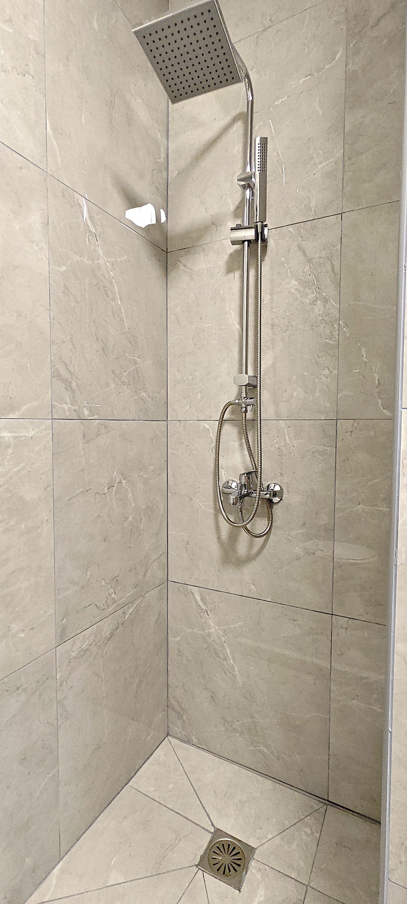 A walk-in shower with a handheld showerhead and a fixed showerhead, tiled walls, and a floor drain.