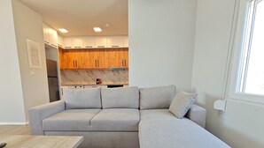 Un salon moderne avec un canapé d’angle gris, une table basse en bois et une cuisine en arrière-plan.