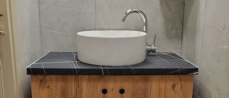 A bathroom with a round mirror, a white sink, and a wooden cabinet.