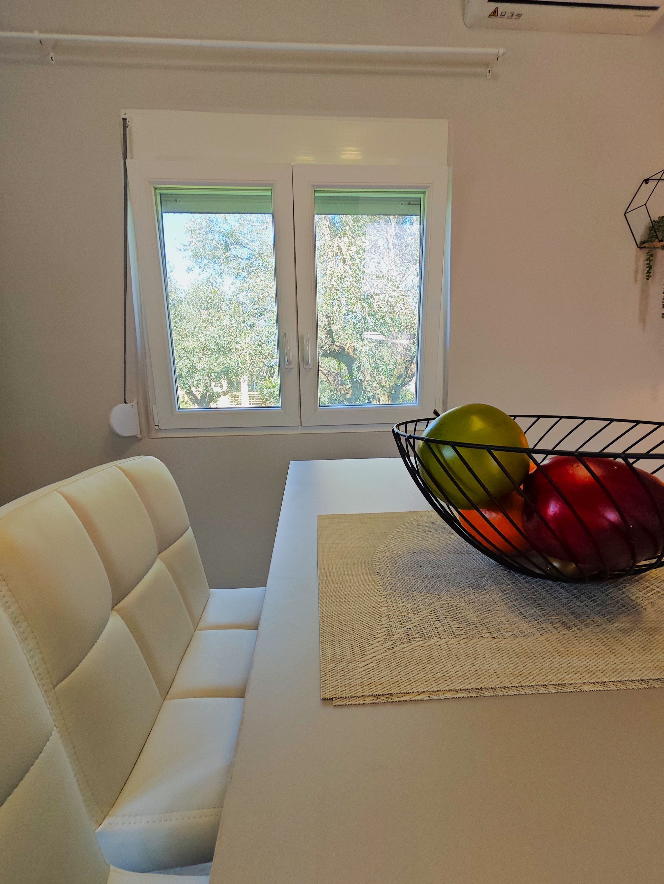 A room with a white sofa, a table with a woven placemat, and a window with a view of trees.