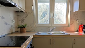 Une cuisine avec un dosseret en marbre, un évier à deux bacs et une fenêtre donnant sur les arbres.
