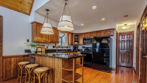 A kitchen with wooden cabinets, a black refrigerator, a bar area with stools, and hanging pendant lights.
