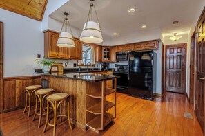 A kitchen with wooden cabinets, a black refrigerator, a bar area with stools, and hanging pendant lights. - Smoky Mountain Views - Fire Pit, Sauna & Hot Tub (Bryson City)