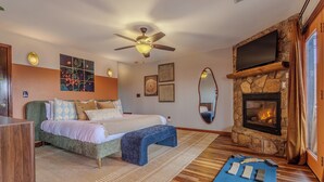 A bedroom with a bed, a ceiling fan, a stone fireplace, and a large mirror.