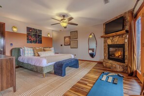 A bedroom with a bed, a ceiling fan, a stone fireplace, and a large mirror. - Smoky Mountain Views - Fire Pit, Sauna & Hot Tub (Bryson City)