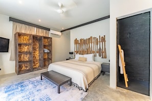 A bedroom with a bed, a wooden wardrobe, a wall-mounted artwork, a black door, and a small bench. - Casa Tribu (Tulum)