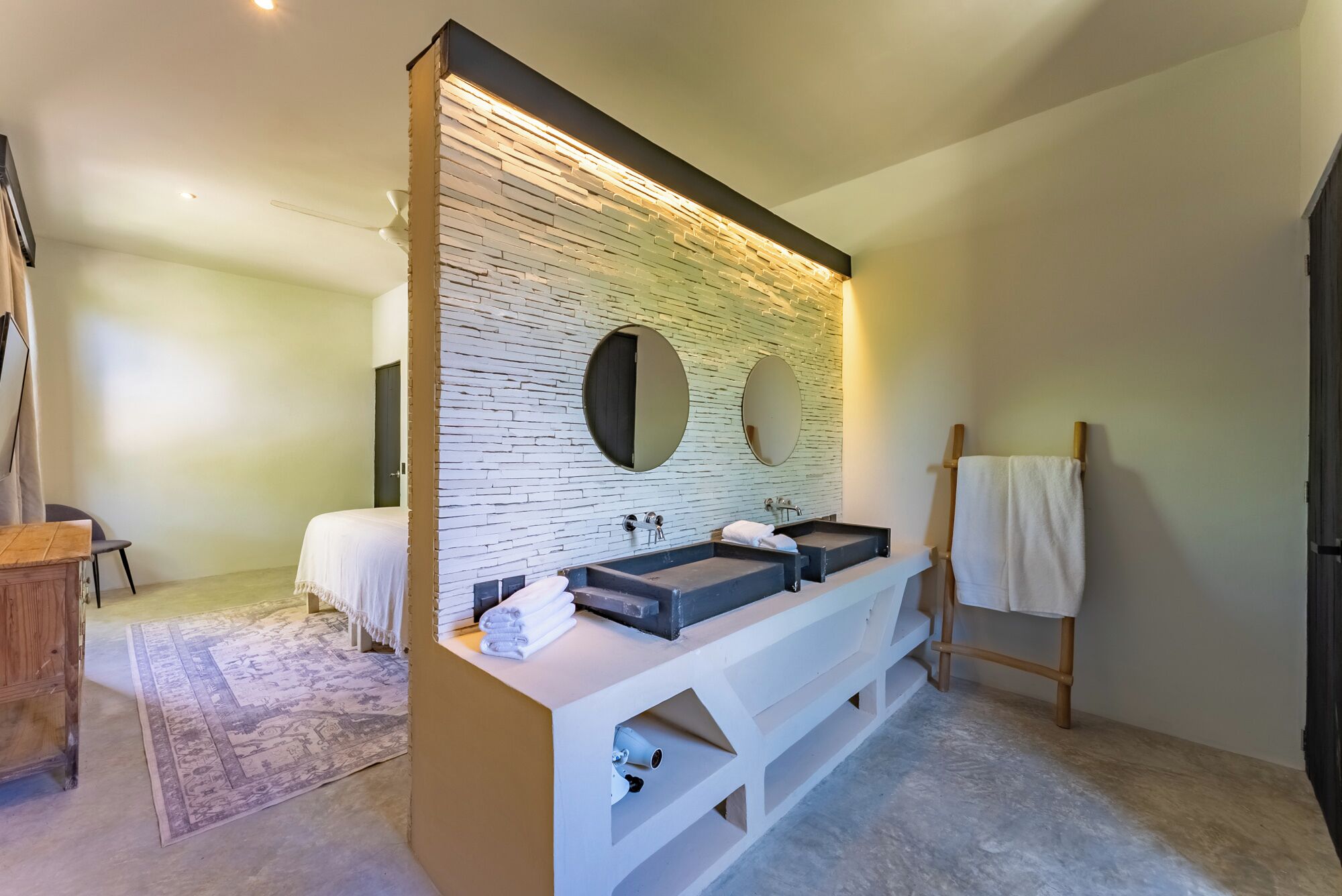 A modern bathroom with a stone wall backsplash, two sinks, and a wooden vanity.