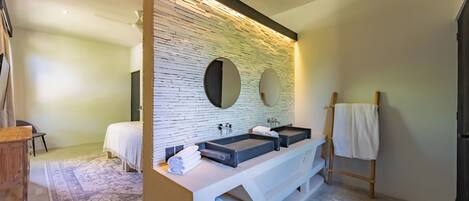 A modern bathroom with a stone wall backsplash, two sinks, and a wooden vanity.