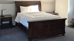 A bedroom with a wooden bed, a nightstand, and a ceiling light fixture. - Gordie's Lookout: Top Floor Loft Suite with Workspace (Alert Bay)