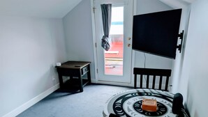 A room with a bed, a small table, a chair, a TV, and a window with curtains. - Gordie's Lookout: Top Floor Loft Suite with Workspace (Alert Bay)