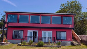 A two-story building with a red exterior, multiple windows, and a small front porch with steps. - Gordie's Lookout: Top Floor Loft Suite with Workspace (Alert Bay)