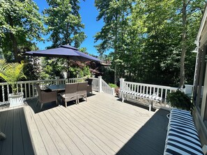 Eine Holzterrasse mit Gartenmöbeln, einem weißen Geländer und einem großen Sonnenschirm.