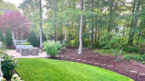 Un jardin bien entretenu, avec une pelouse, un espace détente agrémenté de meubles en osier, ainsi qu’une variété de plantes et d’arbres.