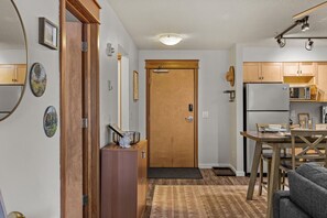 A compact kitchen with wooden cabinets, a refrigerator, a microwave, and a dining area with a table and chairs. - Mountain Getaway| 1 bed 1-Bath Condo (Canmore)