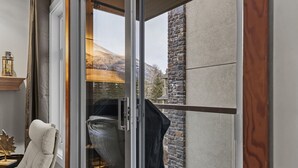 Een kamer met een schuifglasdeur die leidt naar een balkon met een stenen muur en uitzicht op een berg.