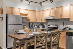 A modern kitchen with wooden cabinets, a stainless steel refrigerator, a built-in oven, and a dishwasher. - Mountain Getaway| 1 bed 1-Bath Condo (Canmore)
