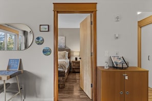 A hotel room with a wooden door leading to a bedroom, a desk with a chair, and a small cabinet. - Mountain Getaway| 1 bed 1-Bath Condo (Canmore)