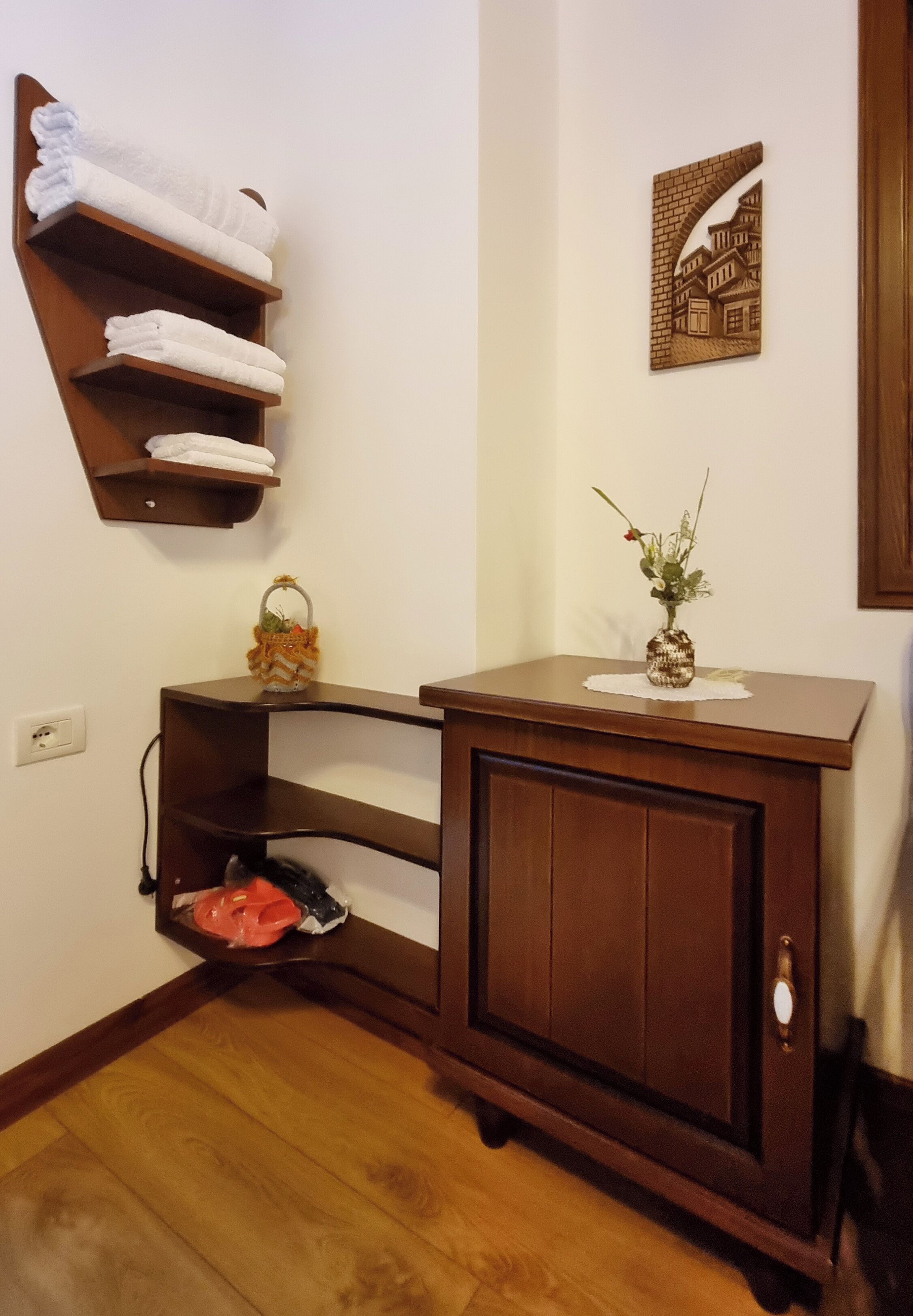 A corner bathroom with a wooden vanity, towel rack, and a decorative wall piece.