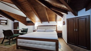 A bedroom with a wooden ceiling, a bed with white bedding, a green chair, a bedside table, and a wardrobe.