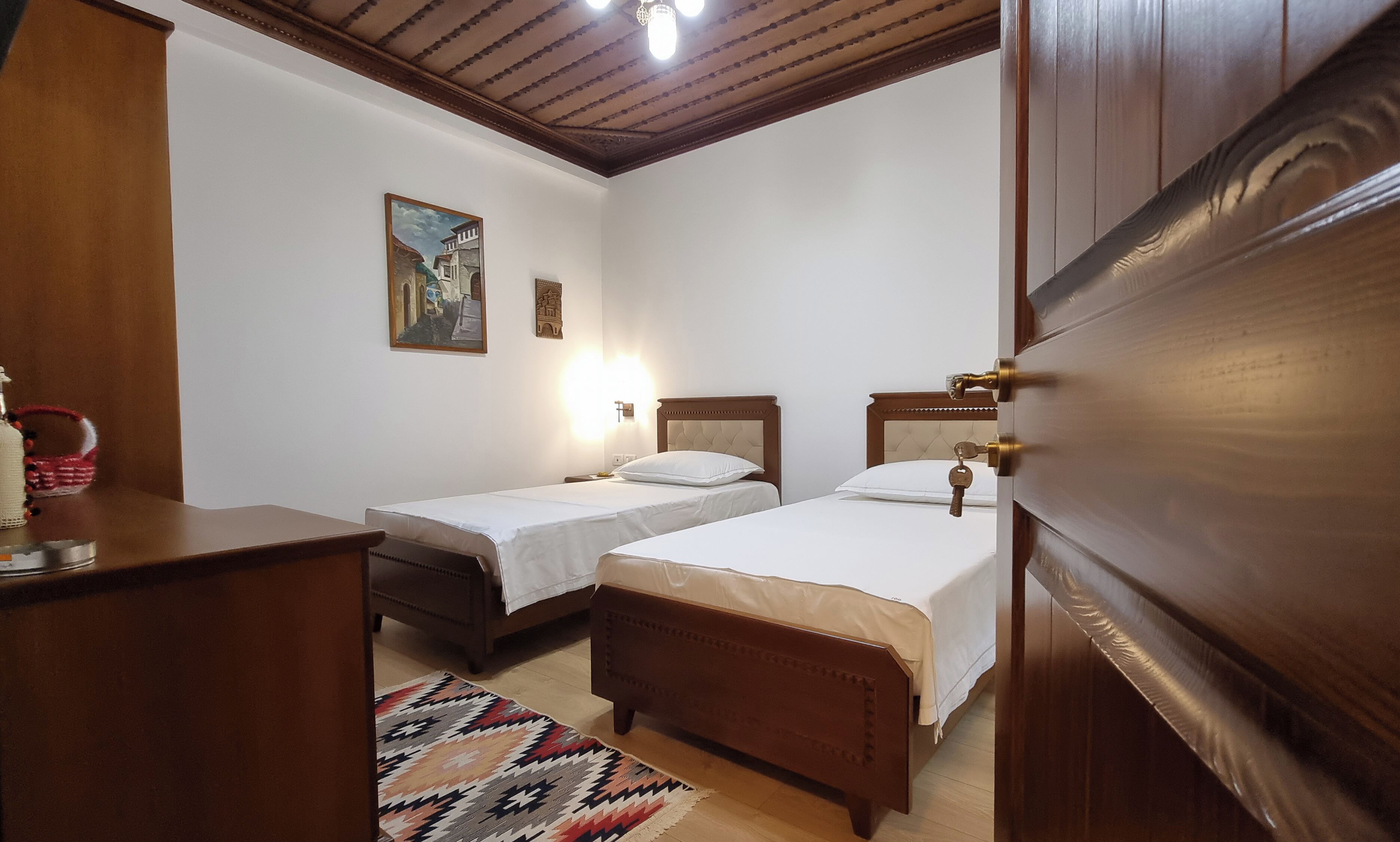 Ein Schlafzimmer mit zwei Betten, einem Holzschrank, einem Nachttisch, einer Lampe und einem Wandbild.