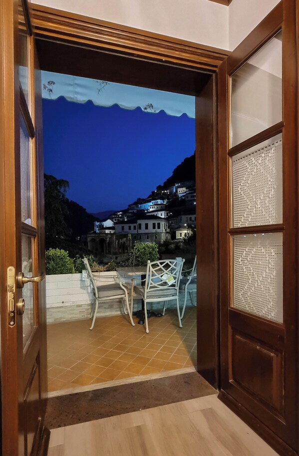 An open door leading to a balcony with a view of a hillside village at dusk.