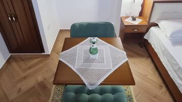 Una habitación acogedora con techo de madera, un sofá verde, una mesa de madera con mantel de encaje, una mesita de noche pequeña y una cama con colcha blanca.