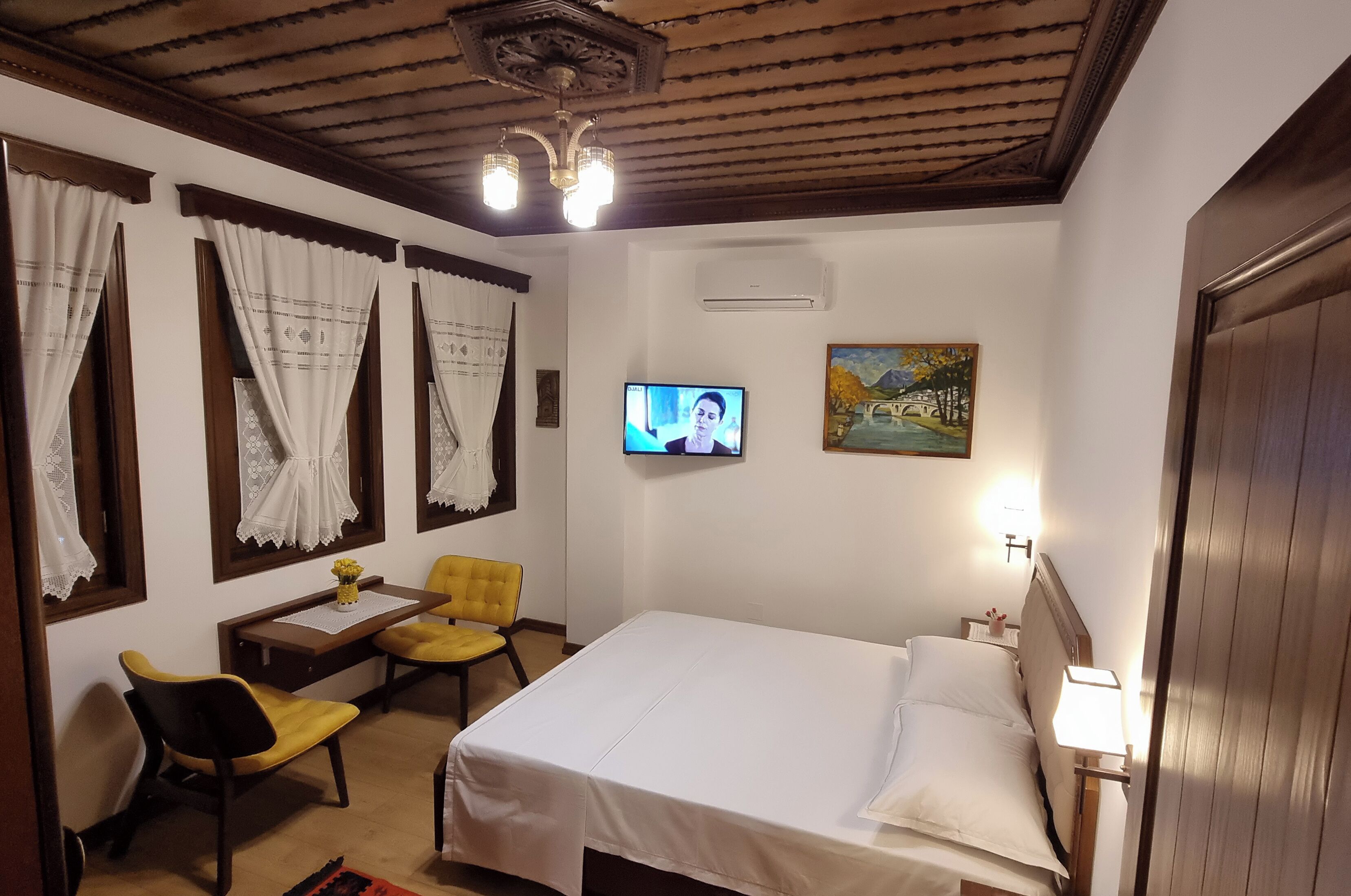A hotel room with a bed, a desk with a chair, a television, and a painting on the wall.