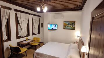 A hotel room with a bed, a desk with a chair, a television, and a painting on the wall.