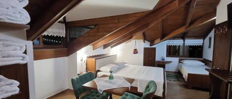 A cozy attic bedroom with a wooden ceiling, a bed, a table with chairs, and a window with lace curtains.