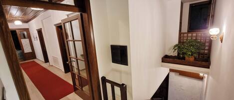A hallway with a red carpet, wooden doors, a staircase, and a window with a plant.