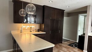 A modern kitchen with dark cabinetry, a large island, pendant lighting, and a neon sign.