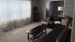 A living room with a dark leather sofa, a coffee table, a TV on a stand, and a lamp.