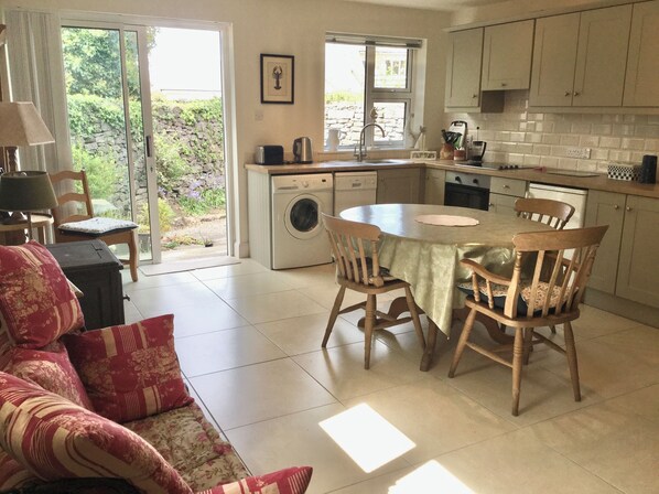 A kitchen with a washing machine, dining table, chairs, and a view of greenery outside.