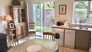 A compact kitchen with a dining area, a washing machine, and a stone wall visible through the door. - Delightful charming townhouse in seaside Ballyvaughan awaits you (Ballyvaghan)